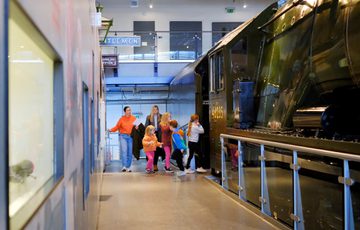 Children and adults explore a large vintage train inside a gallery.