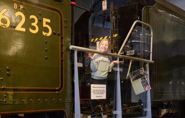 Young girl smiling while standing behind a barrier near a vintage train engine.