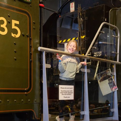 Young girl smiling while standing behind a barrier near a vintage train engine.