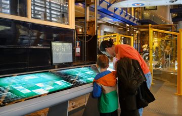 A woman and child explore an interactive exhibit inside a museum with vintage vehicles.