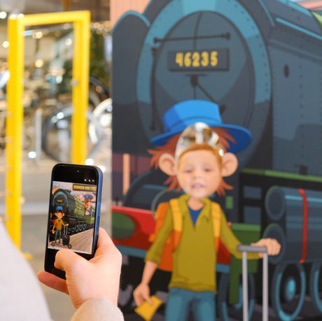 Children posing behind a train-themed cutout, a person person capturing the moment on phone.