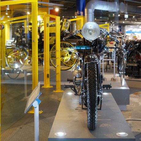 Vintage motorcycle displayed in a museum with yellow-framed glass panels.