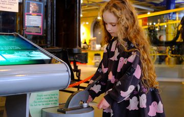 A girl interacts with a museum stamping machine in a gallery setting.