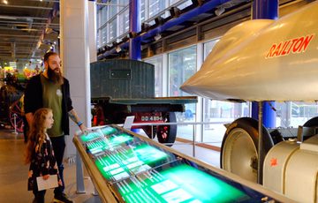 Adult and child looking at the Railton Land Speed vehicle in a gallery.