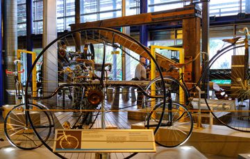 Antique, large-wheeled mechanical bicycles displayed in a museum gallery with informational signage.