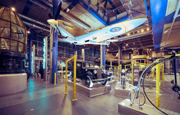 Vintage plane, classic cars, and historical bicycles displayed in an industrial-style gallery.