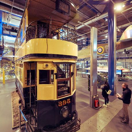 Historic yellow and black tram displayed indoors with visitors observing exhibits nearby.