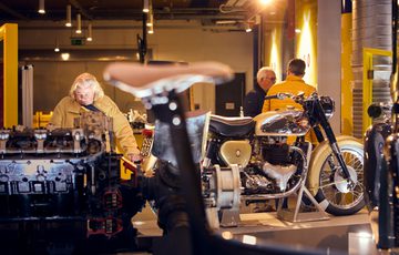 People looking at vintage motorcycles in a museum gallery.
