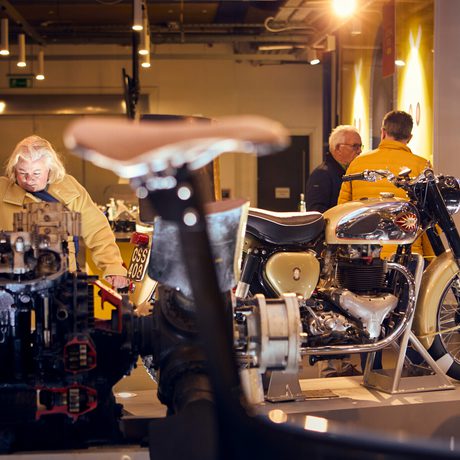 People looking at vintage motorcycles in a museum gallery.