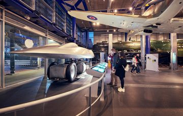 Visitors viewing historical Railton land speed car inside a museum with informational displays.
