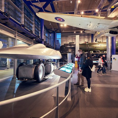Visitors viewing historical Railton land speed car inside a museum with informational displays.