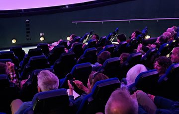A planetarium full of people looking at the screen above.