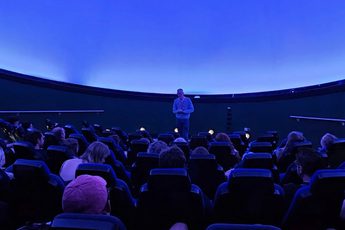 A planetarium full of people looking at a person standing at the front.