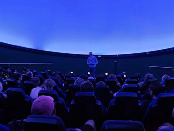 A planetarium full of people looking at a person standing at the front.