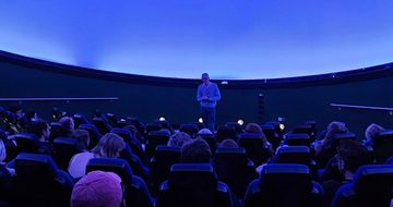 A planetarium full of people looking at a person standing at the front.