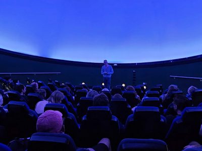 A planetarium full of people looking at a person standing at the front.