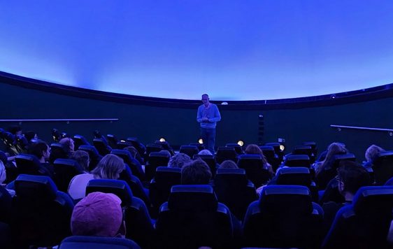A planetarium full of people looking at a person standing at the front.