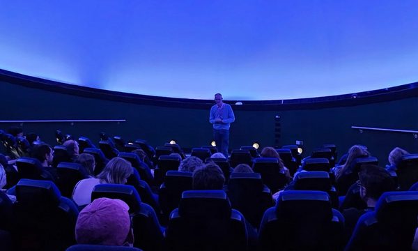 A planetarium full of people looking at a person standing at the front.