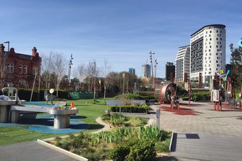 A science garden with trees, plants and science exhibits and two buildings in the distance.