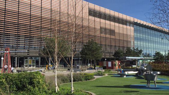 A large modern building with garden in front. In the garden is trees, plants and science exhibits