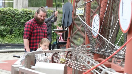 An adult with a child putting balls into a wire tube in the Science Garden.