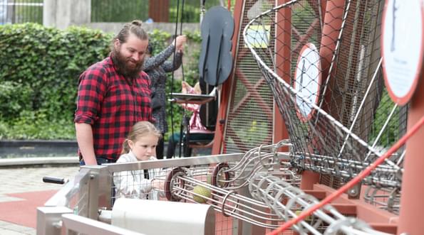 An adult with a child putting balls into a wire tube in the Science Garden.