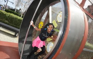 A smiling child on a giant human sized hamster wheel.