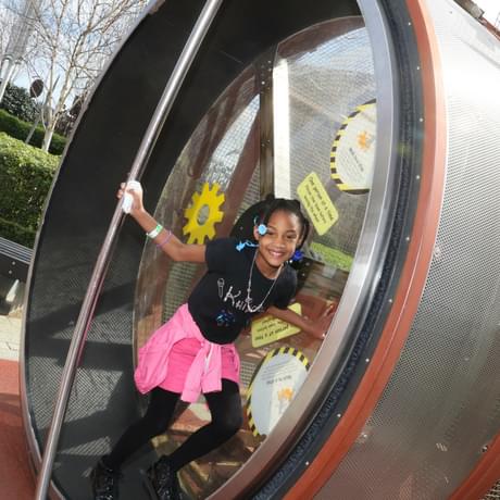 A smiling child on a giant human sized hamster wheel.