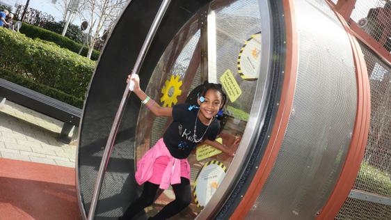 A smiling child on a giant human sized hamster wheel.