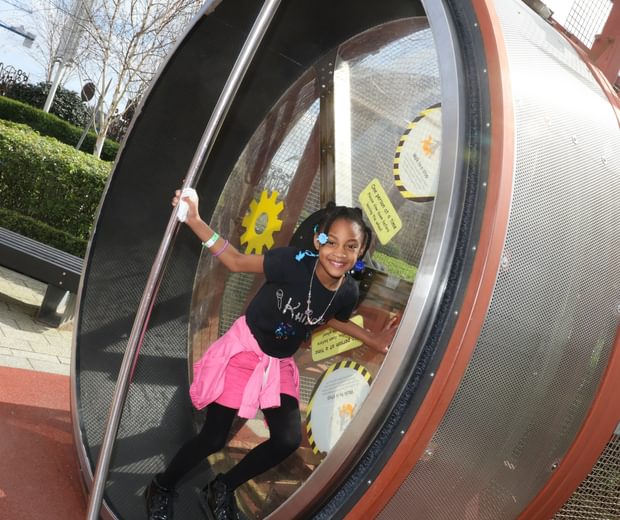 A smiling child on a giant human sized hamster wheel.
