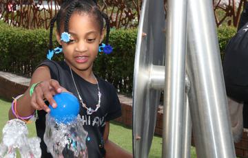 A child balancing a ball on top of an interactive with water shooting up.