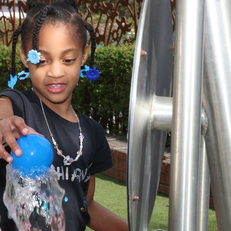 A child balancing a ball on top of an interactive with water shooting up.