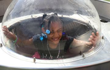 A child in a plastic dome with water running over the top.