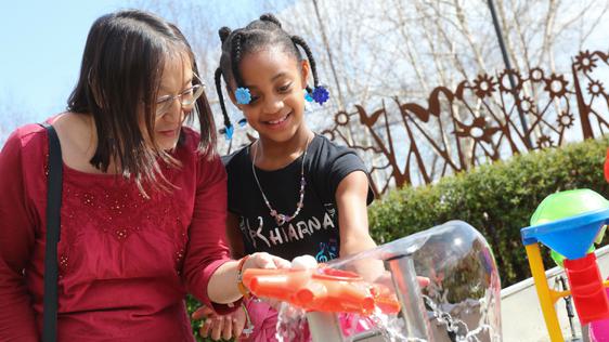 An adult and child playing with an interactive water feature.