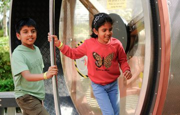 Two children joyfully playing on a large outdoor spinning wheel in the Science Garden.