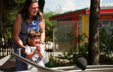 Woman and child smiling, playing on an interactive exhibition on sunny day.