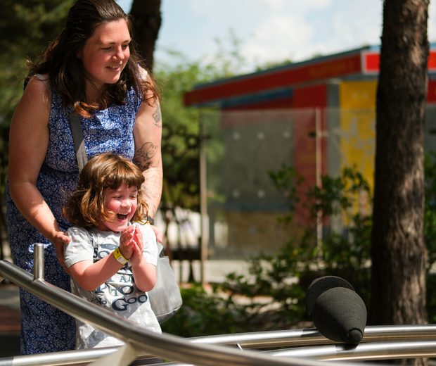 Woman and child smiling, playing on an interactive exhibition on sunny day.