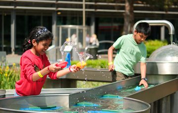 Two children playing with water toys at an outdoor water play station.