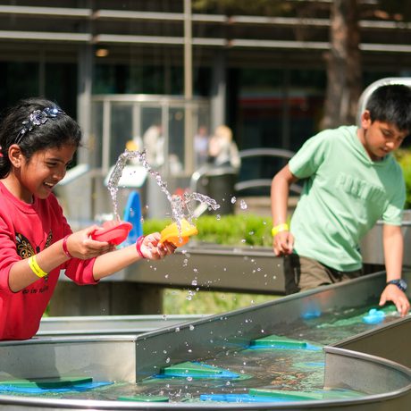 Two children playing with water toys at an outdoor water play station.