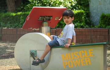 A boy pedals a stationary exercise machine labeled "Muscle Power" in an outdoor Science Garden.