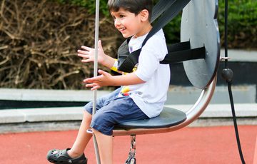 A smiling boy sit joyfully on a chair hoist exhibit.