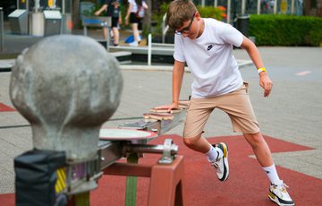 Boy in white shirt and beige shorts interacts with a mechanical exhibit in the Science Garden.