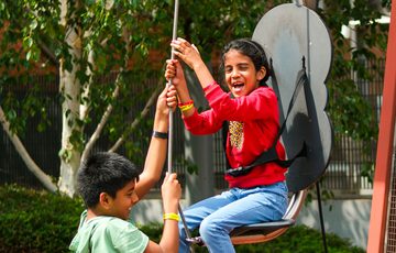 Two children joyfully playing on outdoor hoist and seat.