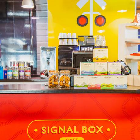 Serving counter of café with railway branding with two jars of biscuits and a stack of tea boxes