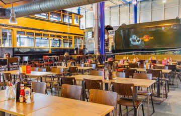 Café dining area in large exhibition hall, an old tram and steam locomotive train are in the background