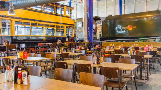 Café dining area in large exhibition hall, an old tram and steam locomotive train are in the background