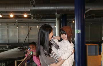 A smiling lady holding a child who is wearing a replica pilot hat.