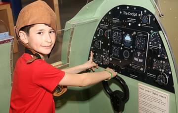 A child sitting in a replica spitfire cockpit.