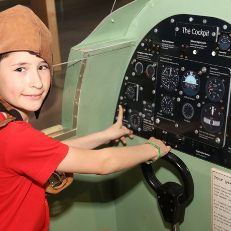 A child sitting in a replica spitfire cockpit.