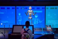 A robot is standing in front of a boy. The robot appears to be talking or singing.